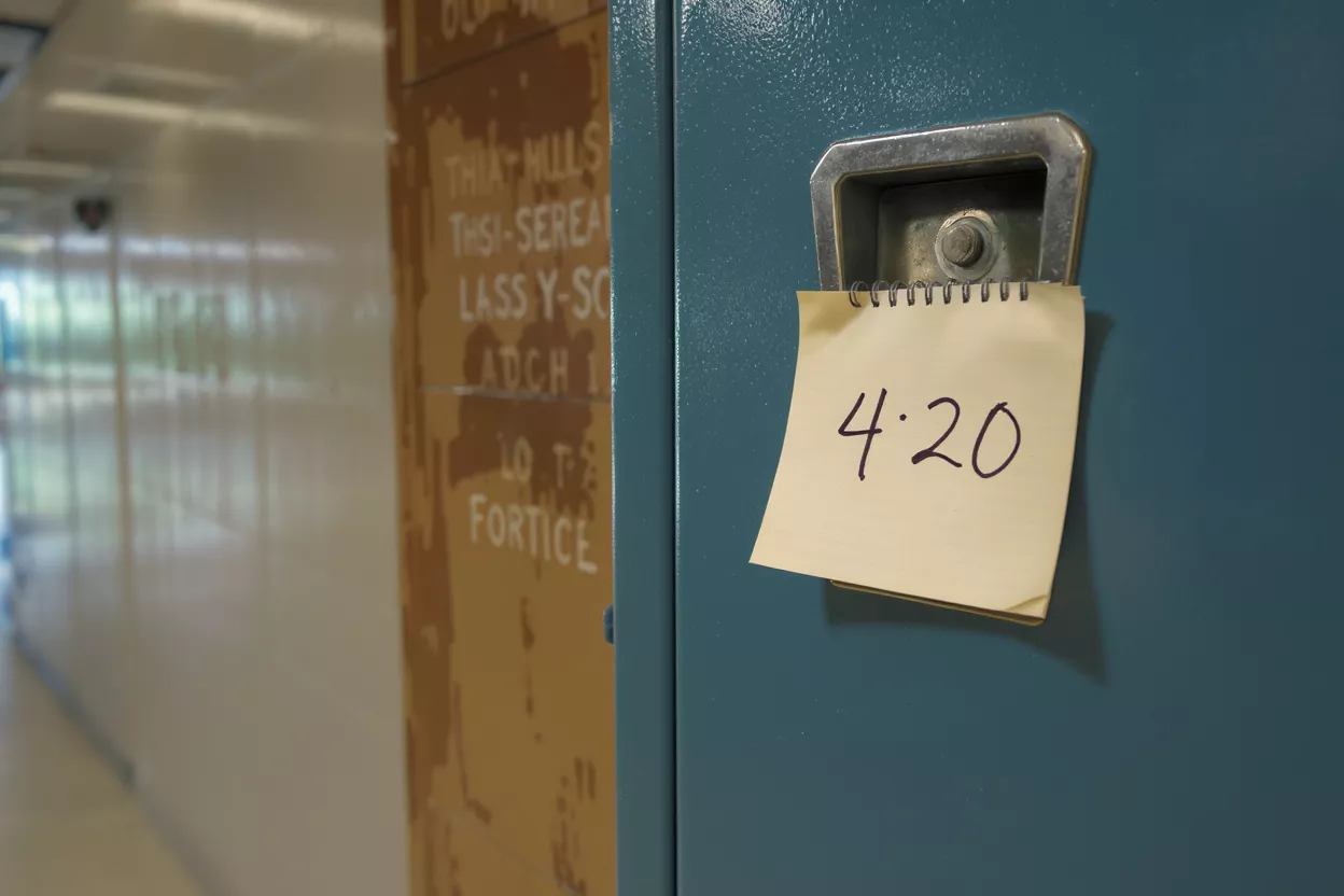 A close-up of a blue locker with a handwritten note reading '4·20' hanging from it.