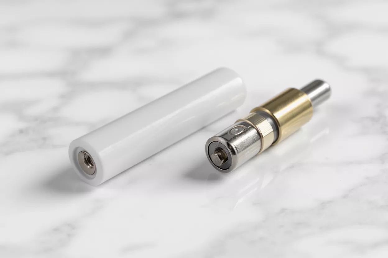 A white vape pen battery next to a metallic atomizer cartridge on a marble background.