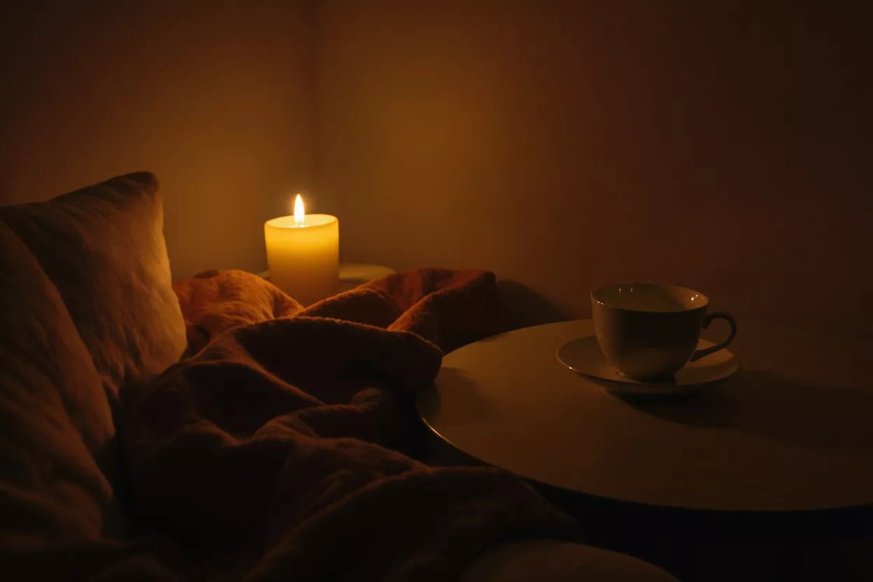 Cozy Candlelight Tea Moment A warm, glowing candle illuminates a bedside scene with a teacup.
