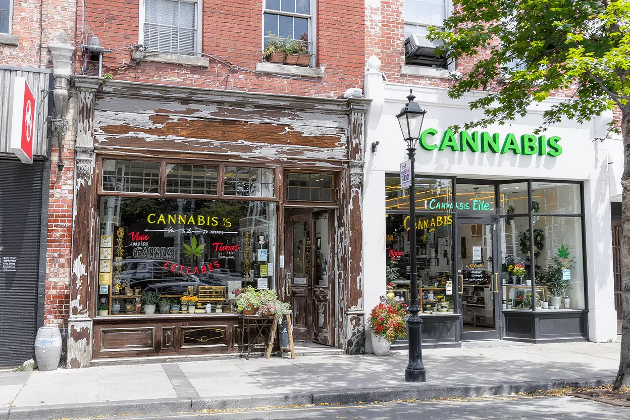 Cannabis Stores Street Front Two cannabis stores side-by-side on a city street with brick and white facades.