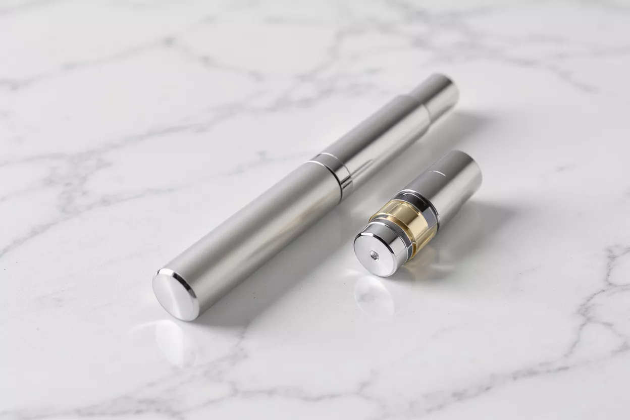 Un stylo vape argenté et une cartouche aux reflets dorés sur une surface en marbre blanc.