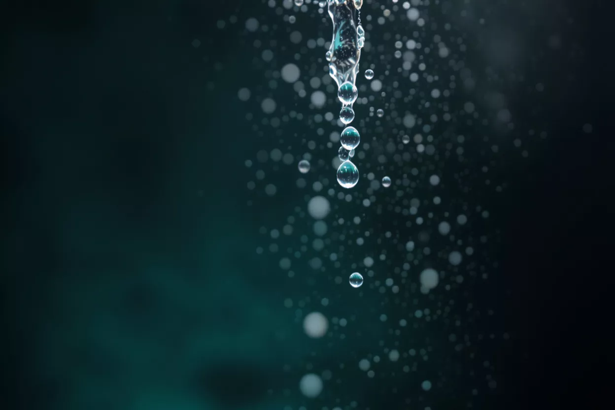 Close-up of water drops falling against a dark, teal-tinged background.