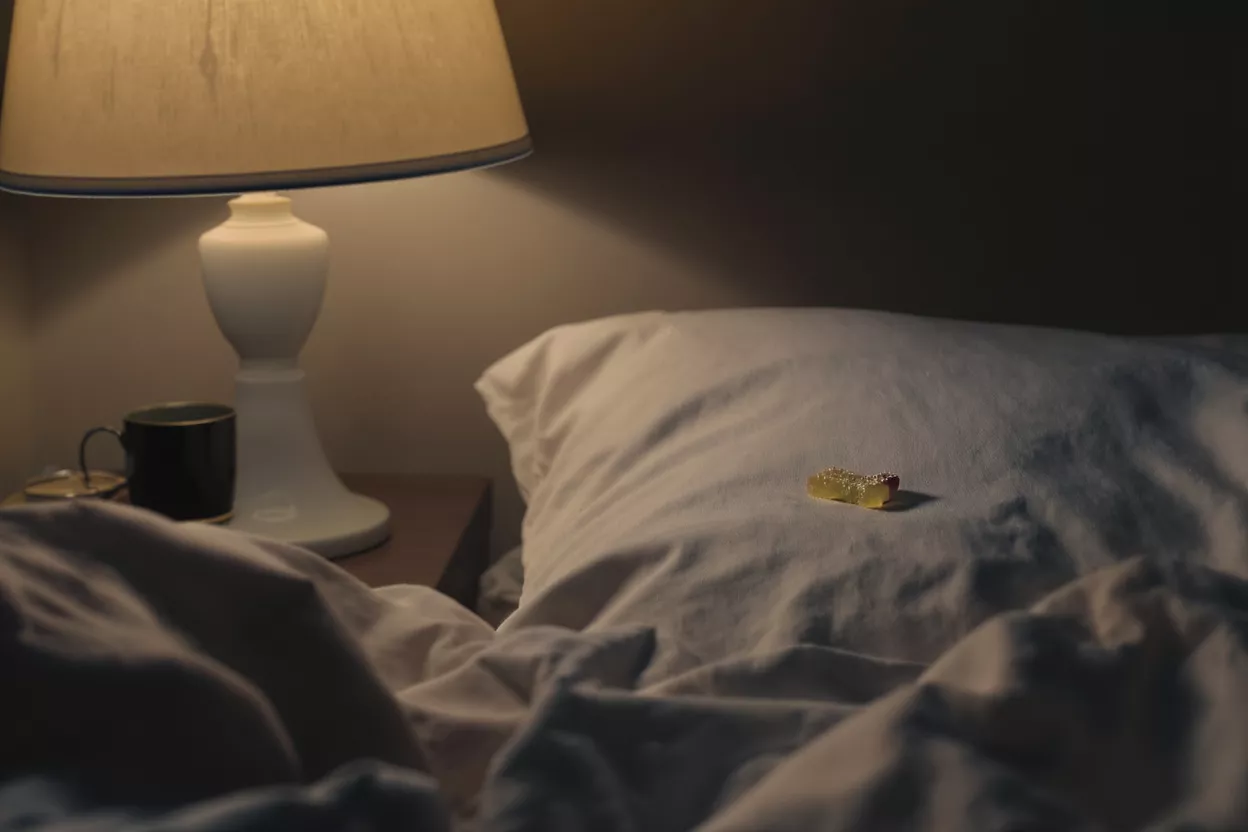 Una golosina de goma descansa sobre una almohada blanca junto a una lámpara de mesita encendida.