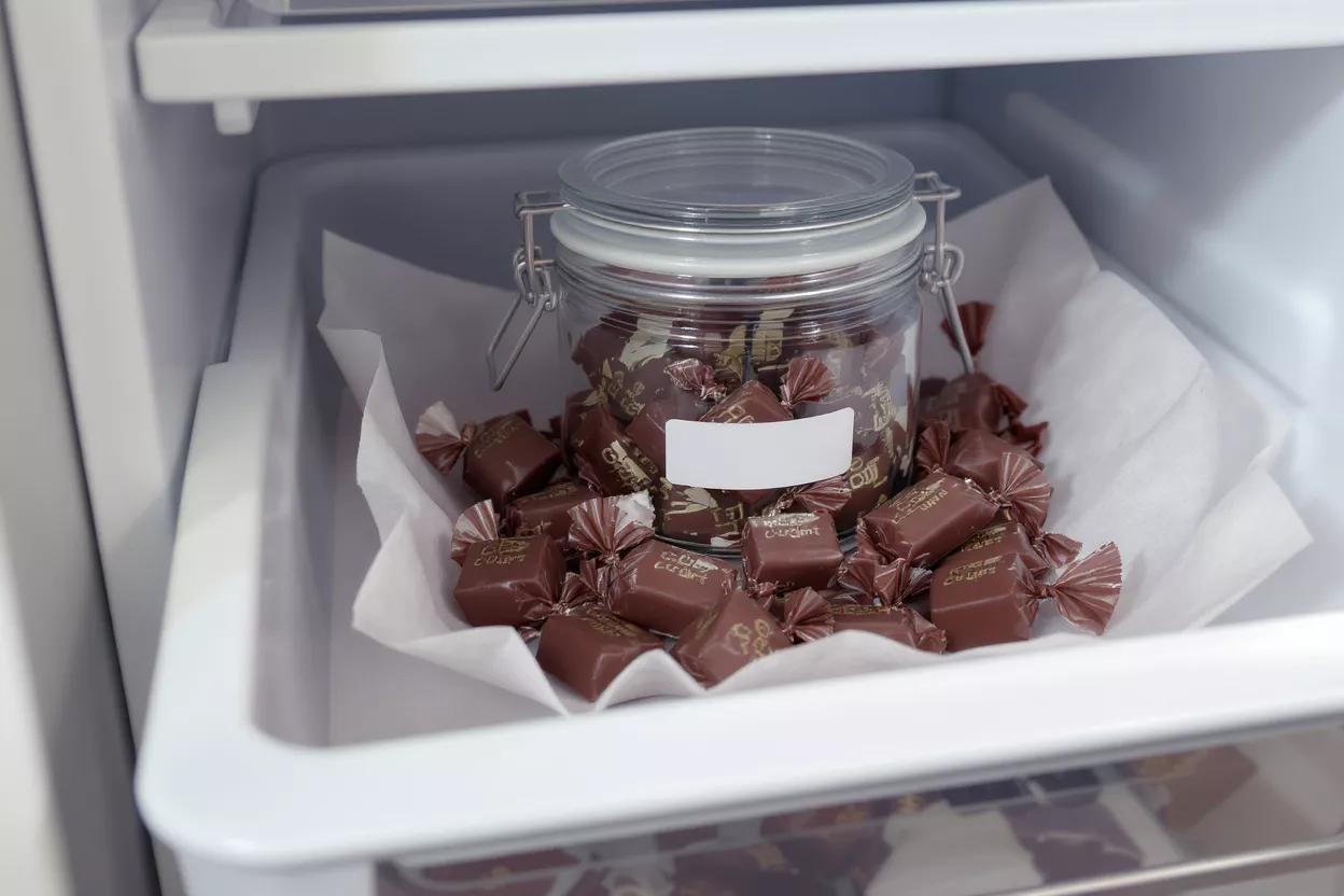 Chocolate candies in a glass jar and scattered in a refrigerator drawer.