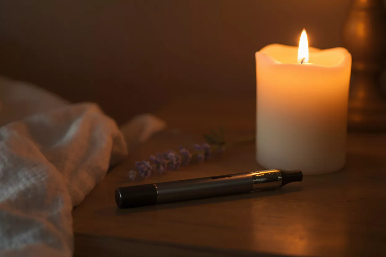 Vape pen, lit candle, and lavender sprig on a wooden surface, creating a relaxing ambiance.
