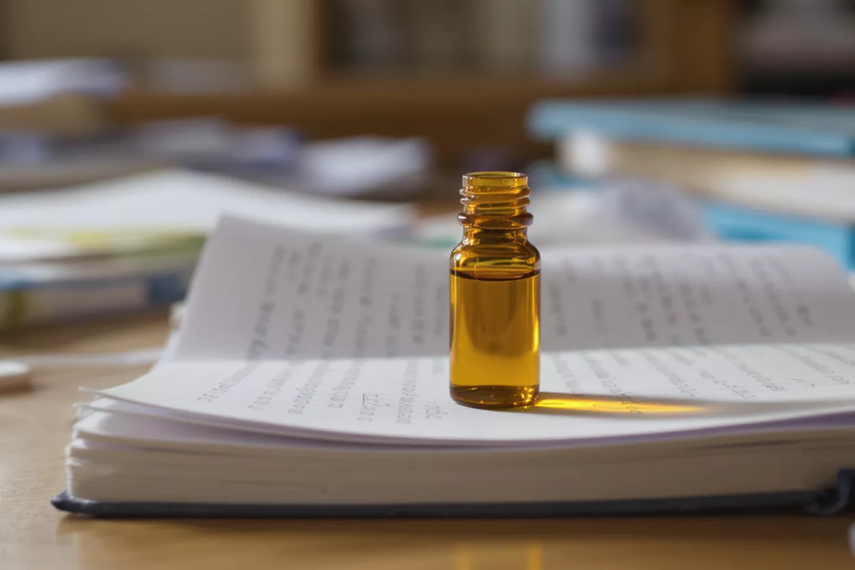 Small amber glass bottle with liquid on an open book, blurred background.