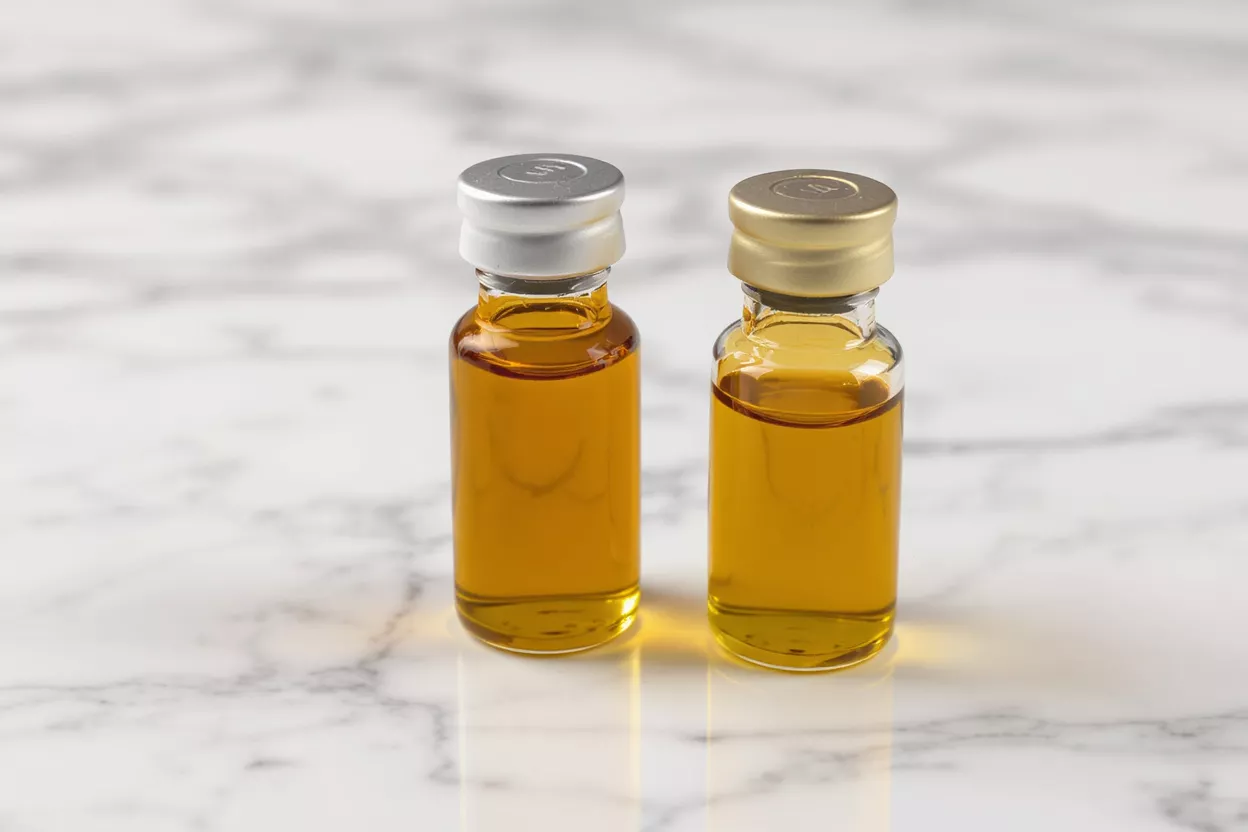 Two small glass vials with amber liquid and metallic caps on a marble surface.