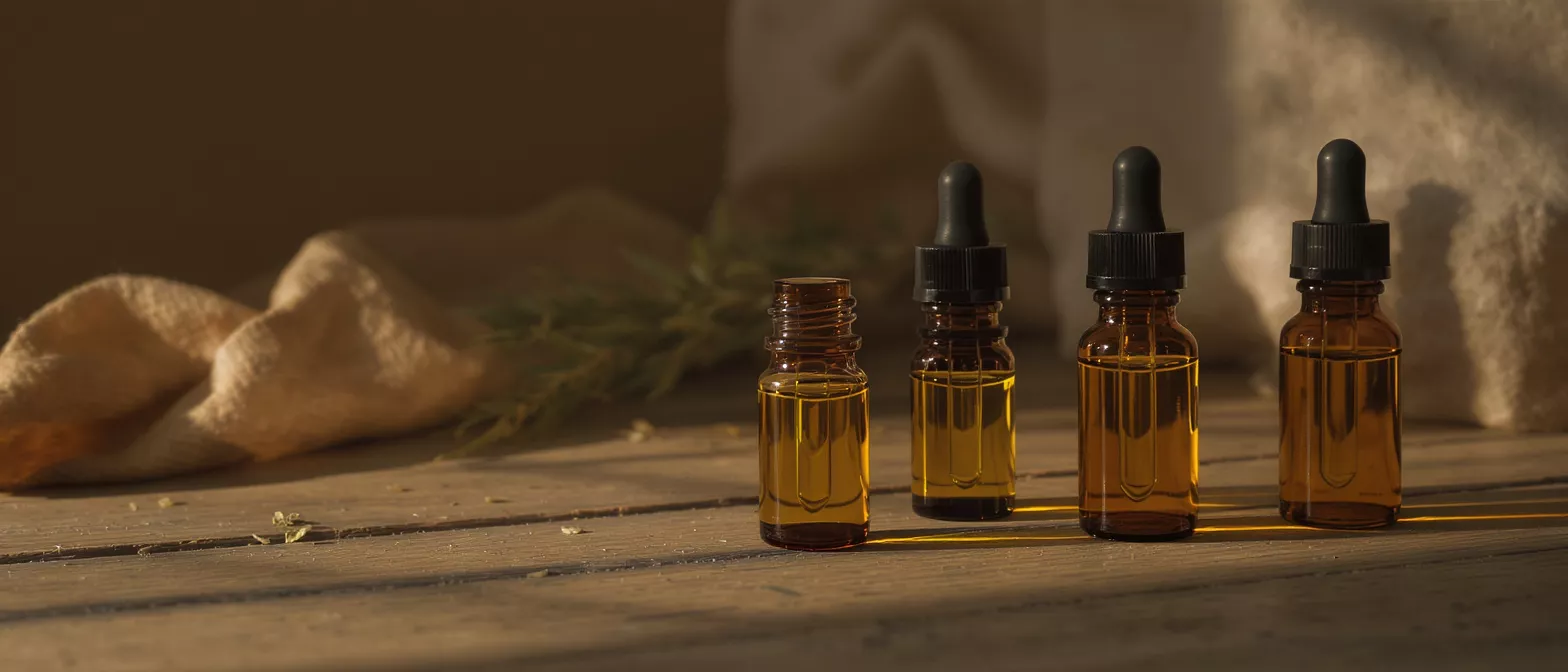Four amber dropper bottles filled with golden liquid on a rustic wooden surface.