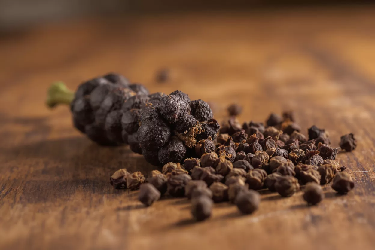 Cubeb pepper berries and a dried cubeb fruit on a rustic wooden surface.