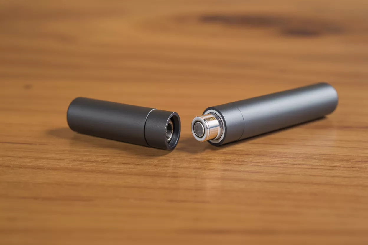 Un stylo vape gris, démonté en deux parties, reposant sur une table en bois.