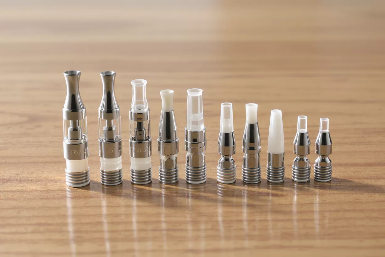 A row of various vape tanks and mouthpieces on a wooden surface.