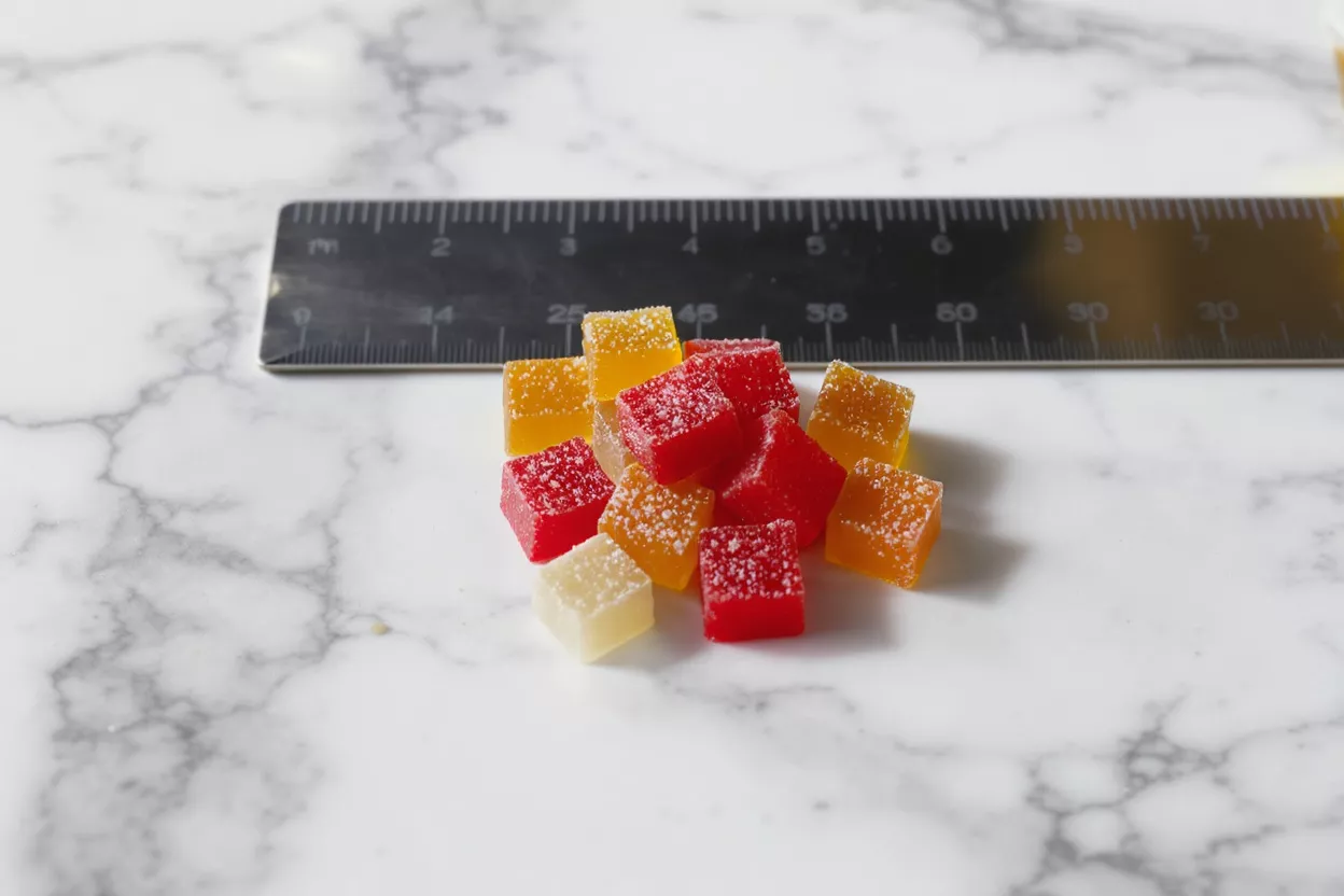 A pile of red, orange, and white sugar-coated gummy cubes on a marble surface.