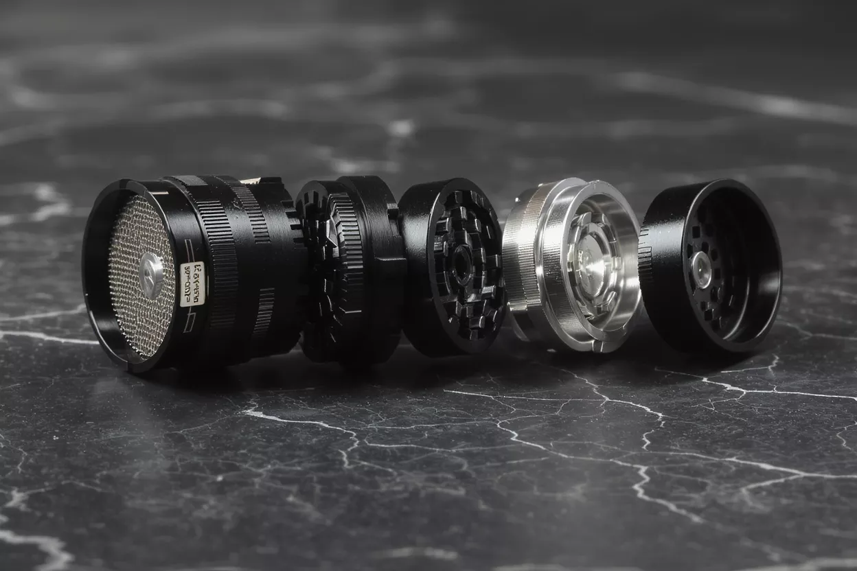 A black and silver grinder disassembled into five parts on a dark marble surface.
