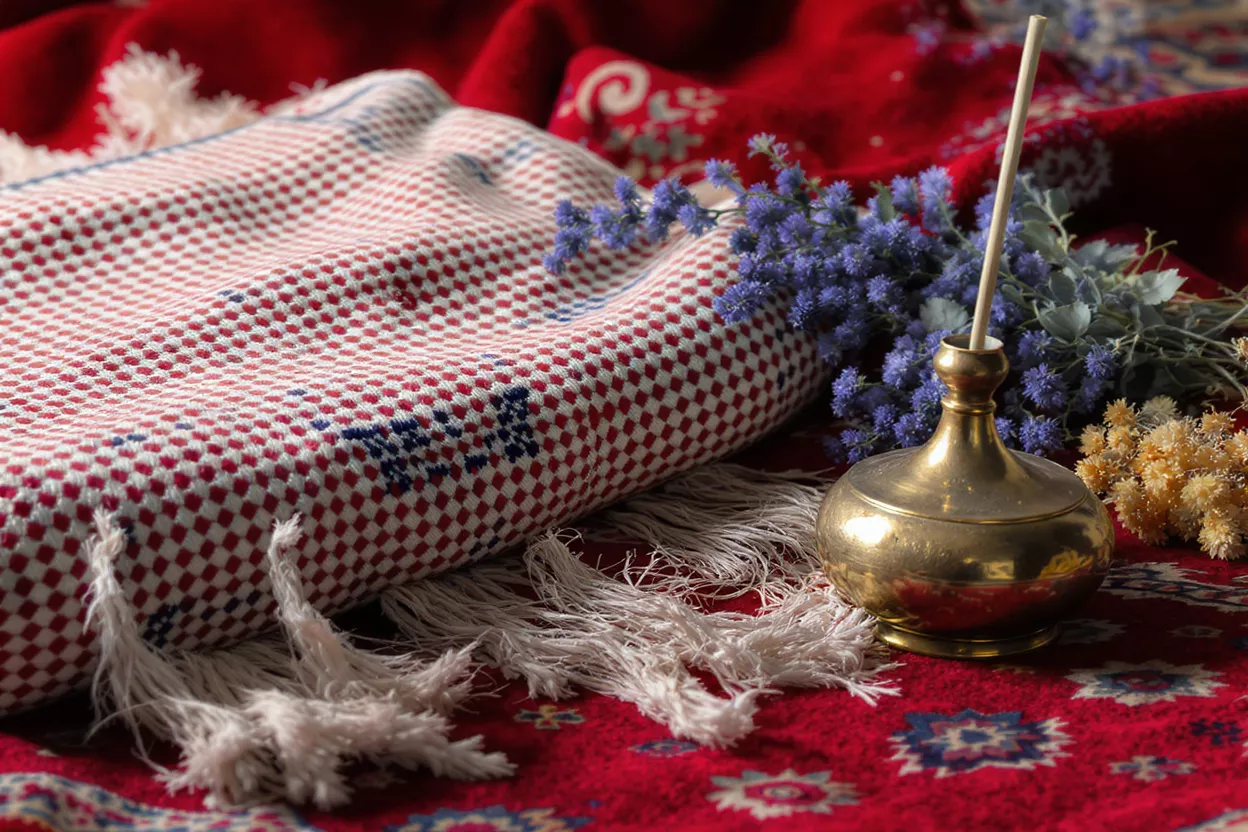 Red and white checkered textile with tassels, brass incense holder, and dried flowers.