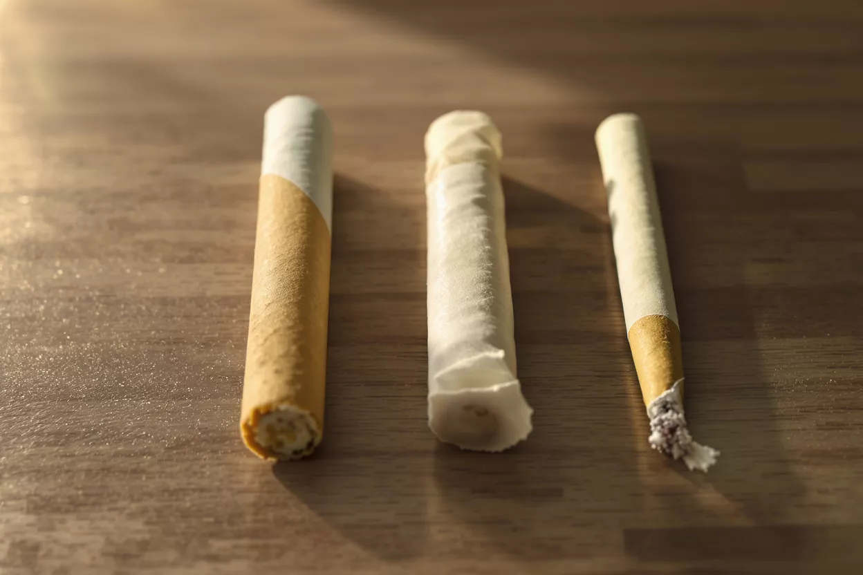 Three Cigarettes on Wood Three cigarettes, one with a filter, one crumpled, and one partially smoked, on wood.