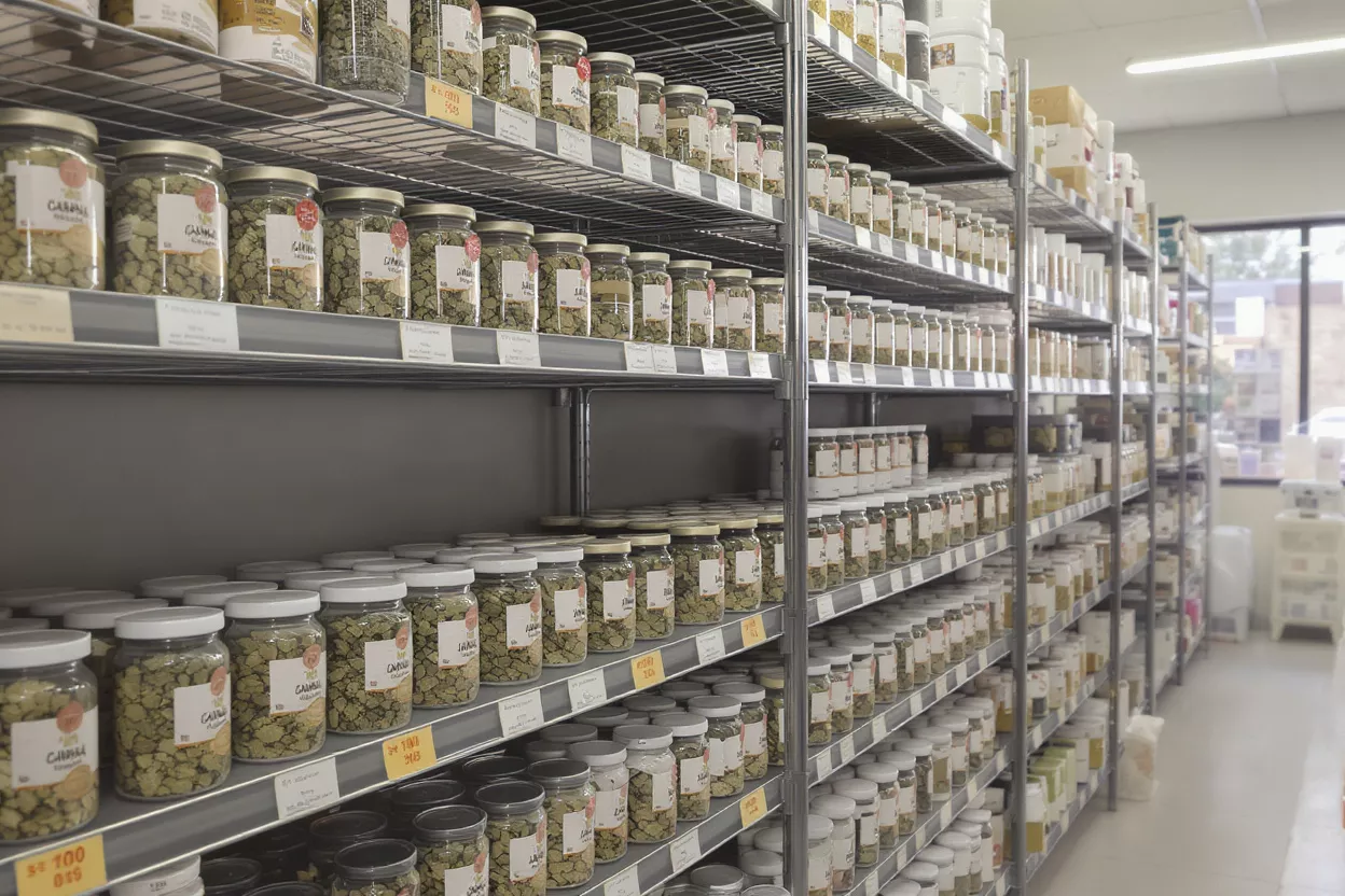 Rows of glass jars filled with dried herbs on metal shelves in a store.