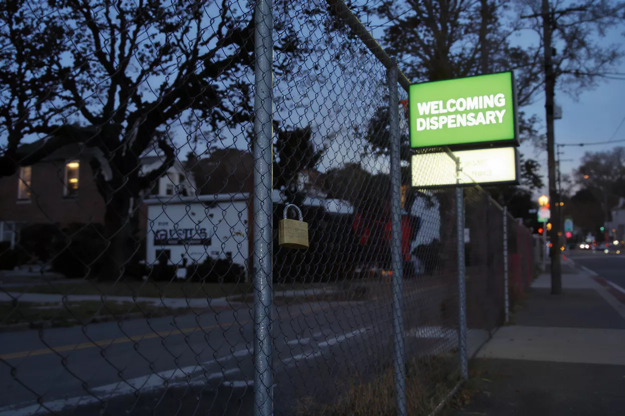 A chain-link fence with a padlock, in front of a 'Welcoming Dispensary' sign.