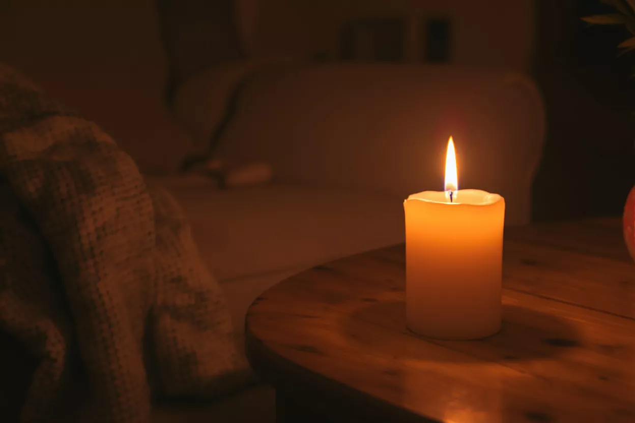 A single lit candle on a wooden table in a dimly lit, cozy room.