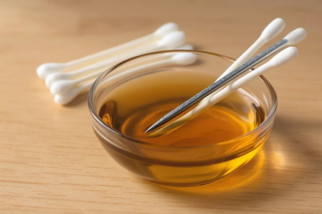 Q-tips and a glass bowl with oil on a wooden surface.