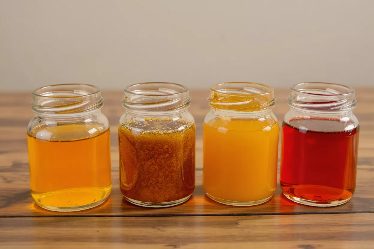 Four small glass jars with different colored liquids on a wooden surface.