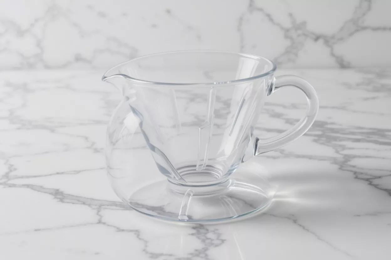 A clear glass pour-over coffee dripper with an integrated server on a marble countertop.