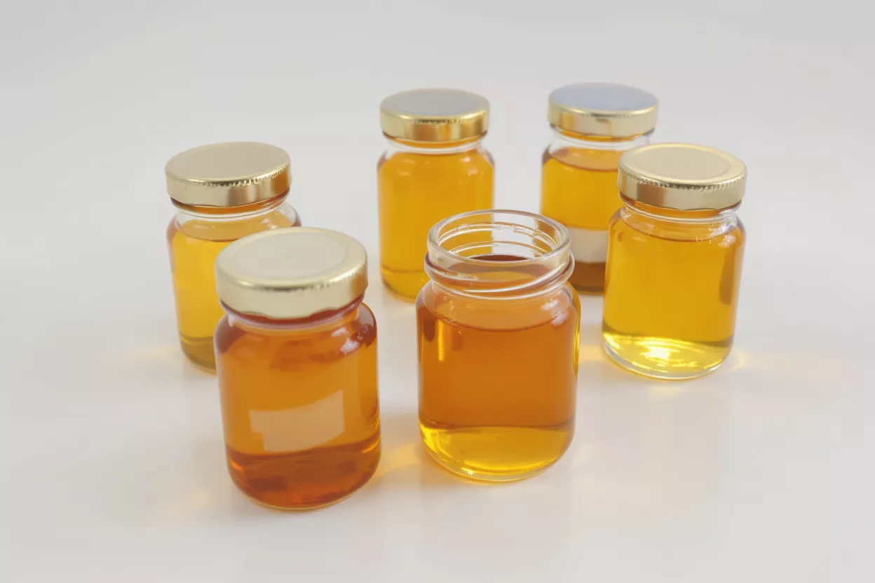 Six small glass jars filled with golden honey on a white background.