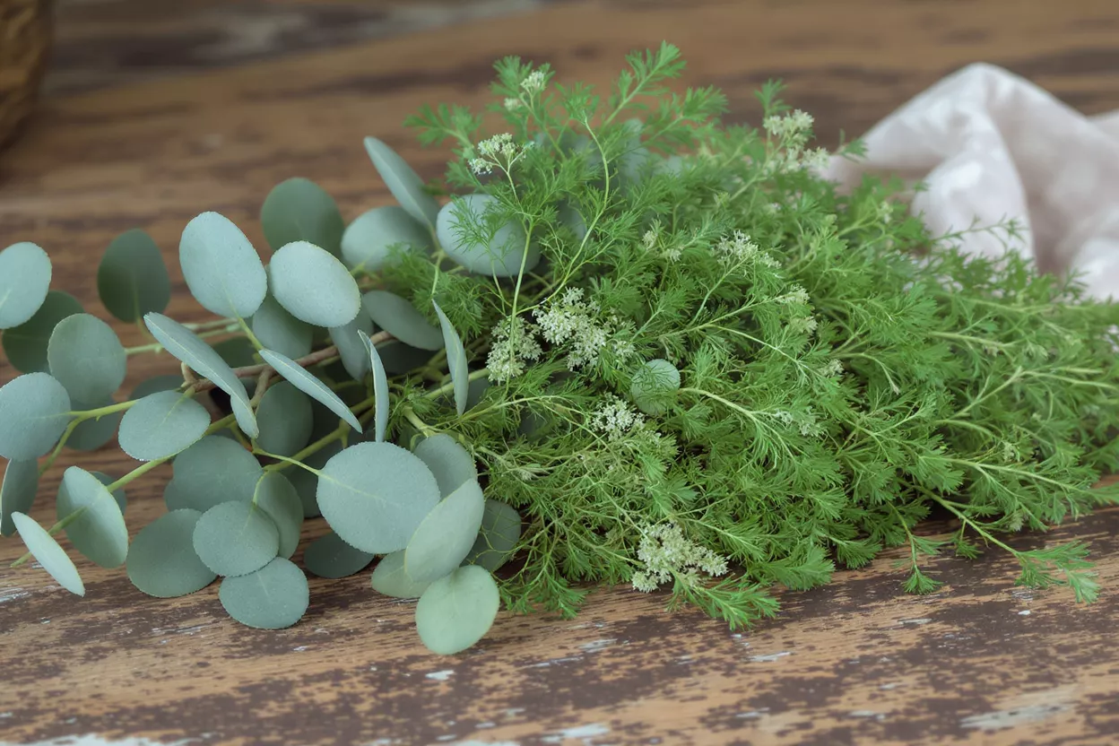 A rustic bouquet of eucalyptus and feathery green foliage on a wooden surface.
