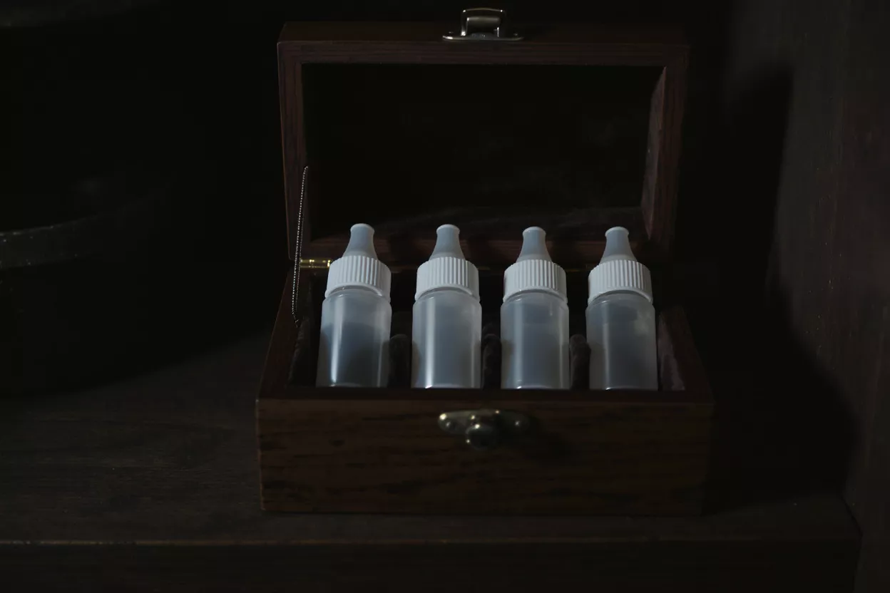 Four small, clear plastic dropper bottles with white caps in an open wooden box.