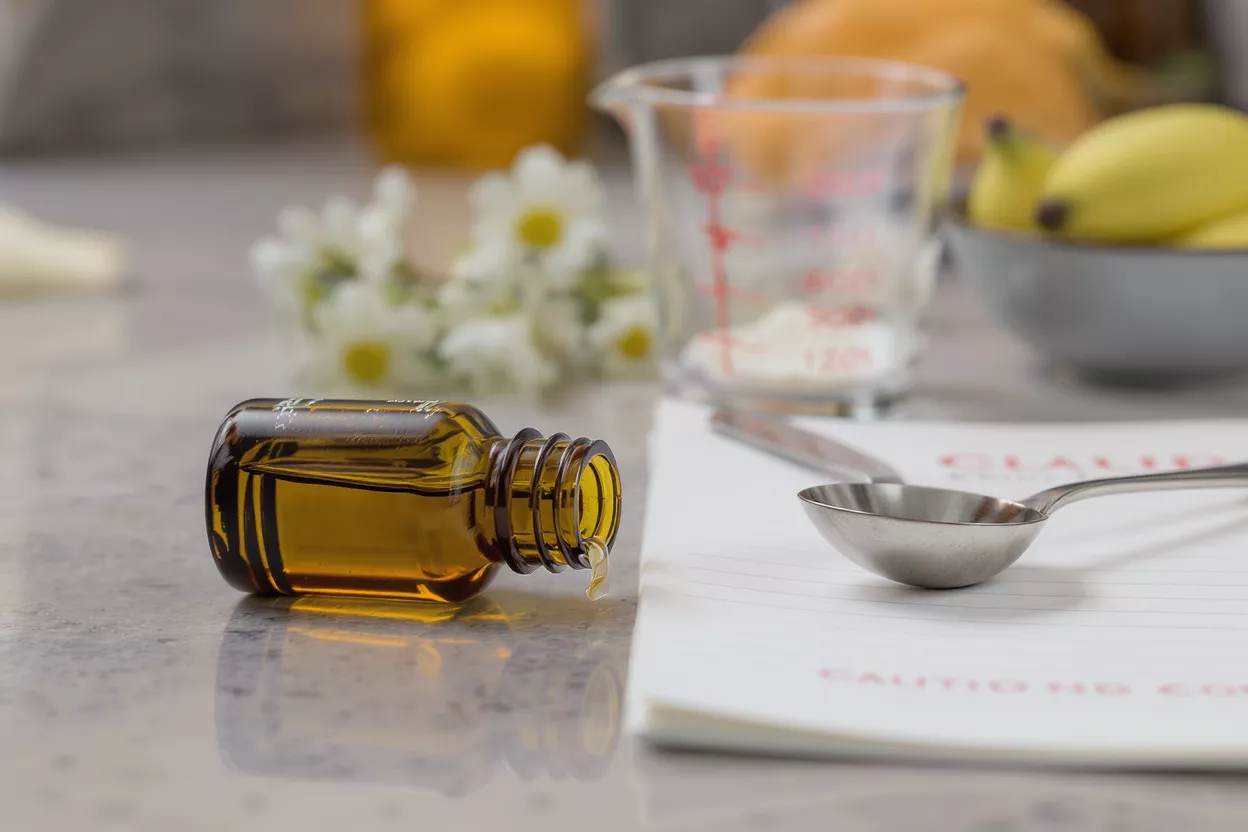 Amber essential oil bottle dripping liquid onto a measuring spoon on a counter.