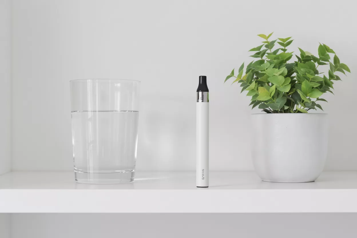 White vape pen, glass of water, and potted plant on a white shelf.
