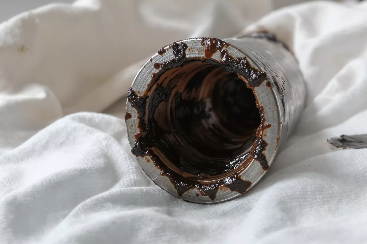Close-up of a metal pipe's interior, heavily coated with dark, thick grease.