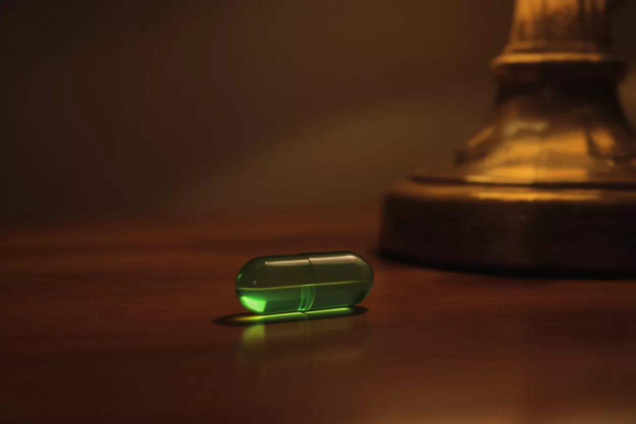 Glowing Green Pill A glowing green pill lies on a dark wooden surface, illuminated by a warm light.