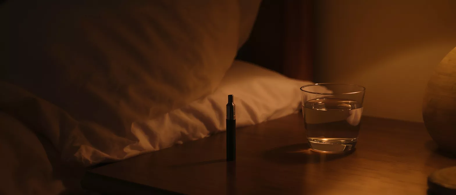 Vape Pen on Bedside Table A vape pen and glass of water on a bedside table in dim light.