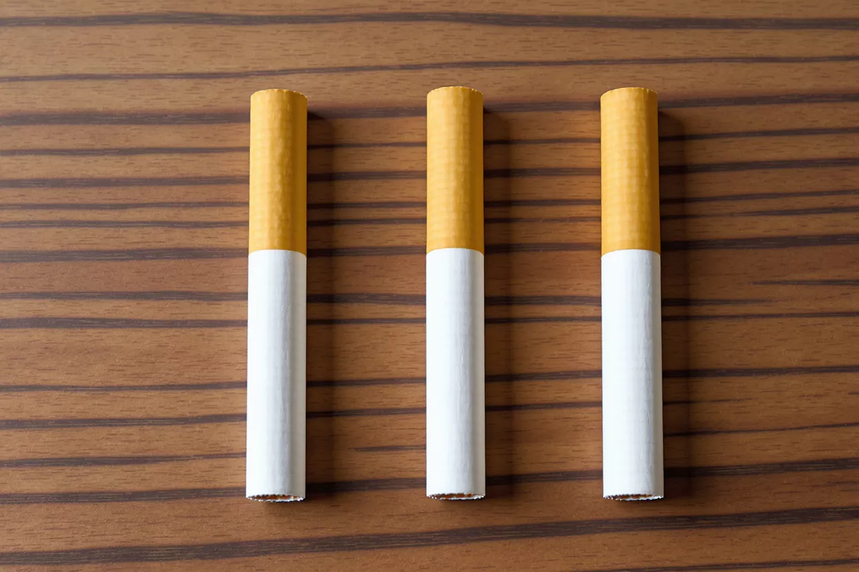 Three unlit cigarettes with yellow filters on a striped wooden surface.