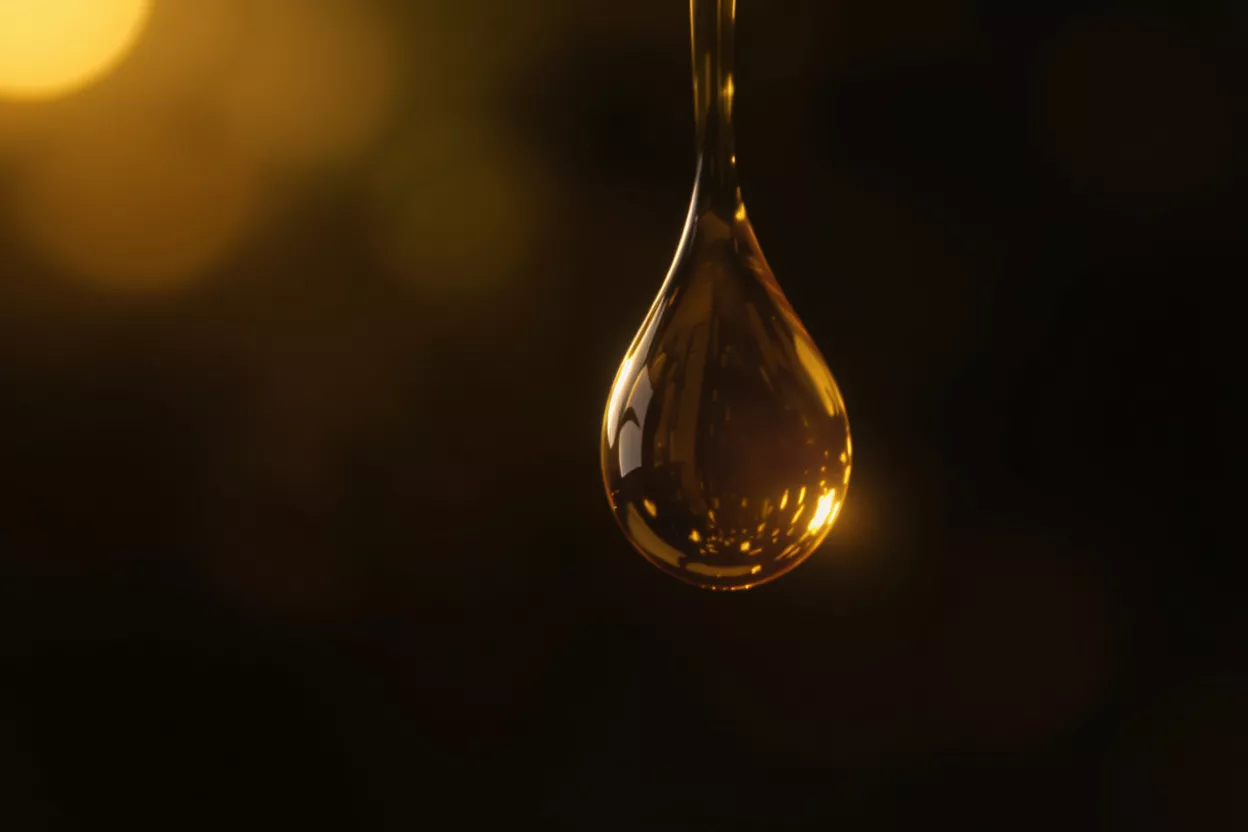 A single drop of golden oil against a dark background