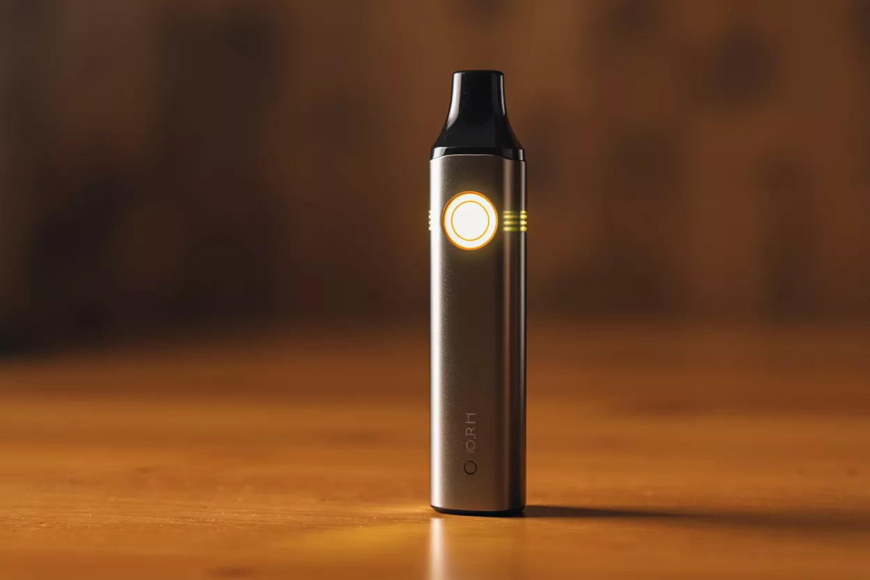 Élégant appareil à vapotage Un appareil à vapotage moderne et métallique avec un voyant jaune lumineux sur une surface en bois.