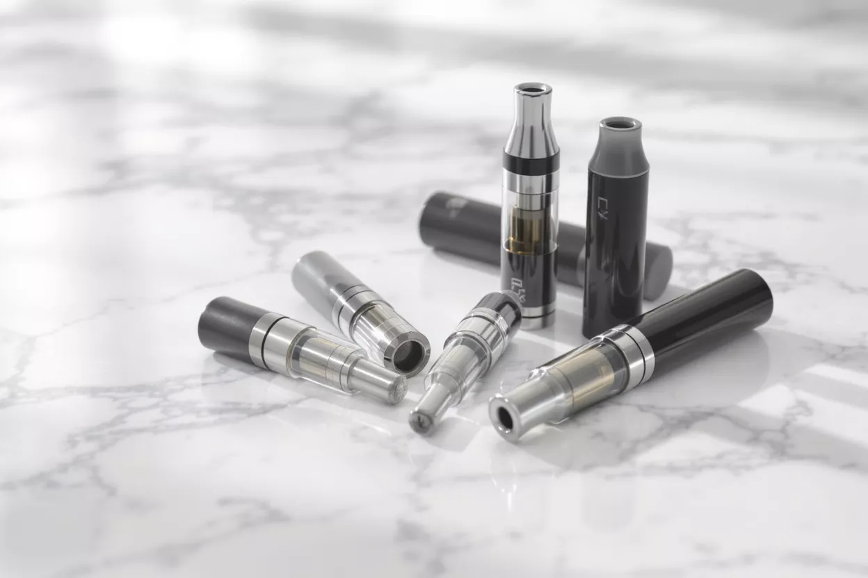 Cartouches et pods pour vapoteuse Plusieurs cartouches et pods pour vapoteuse sur une surface en marbre blanc, certains debout, d'autres couchés.