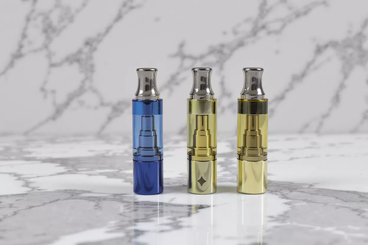 Three vape tanks: one blue, two gold, on a marble background.