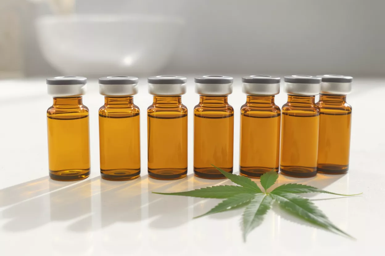 Seven amber vials of CBD oil and a green cannabis leaf on a white surface.
