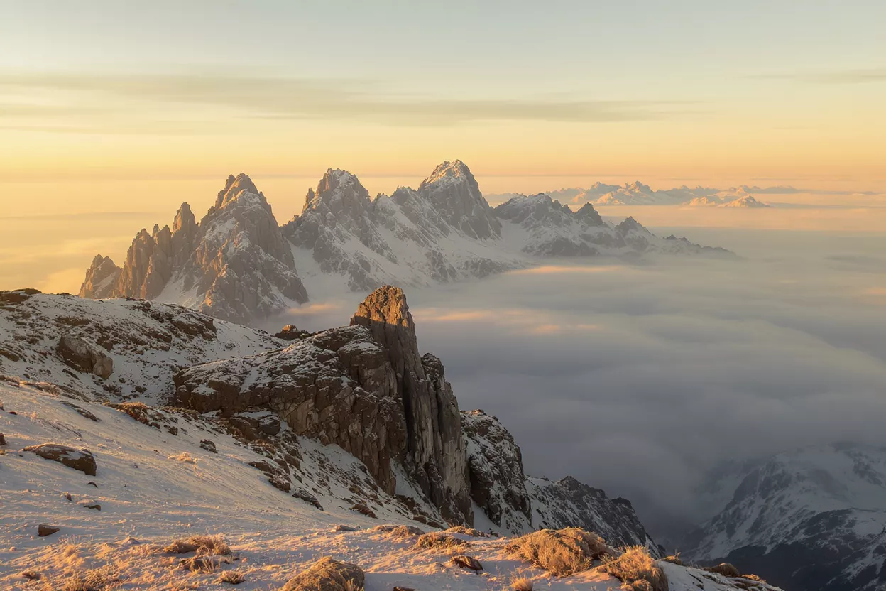 Snow-capped mountain peaks emerging from a sea of clouds at sunrise.