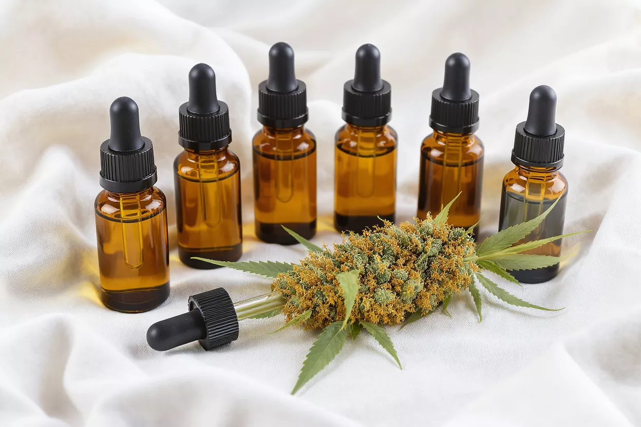 Six amber dropper bottles of CBD oil with a cannabis flower on white fabric.