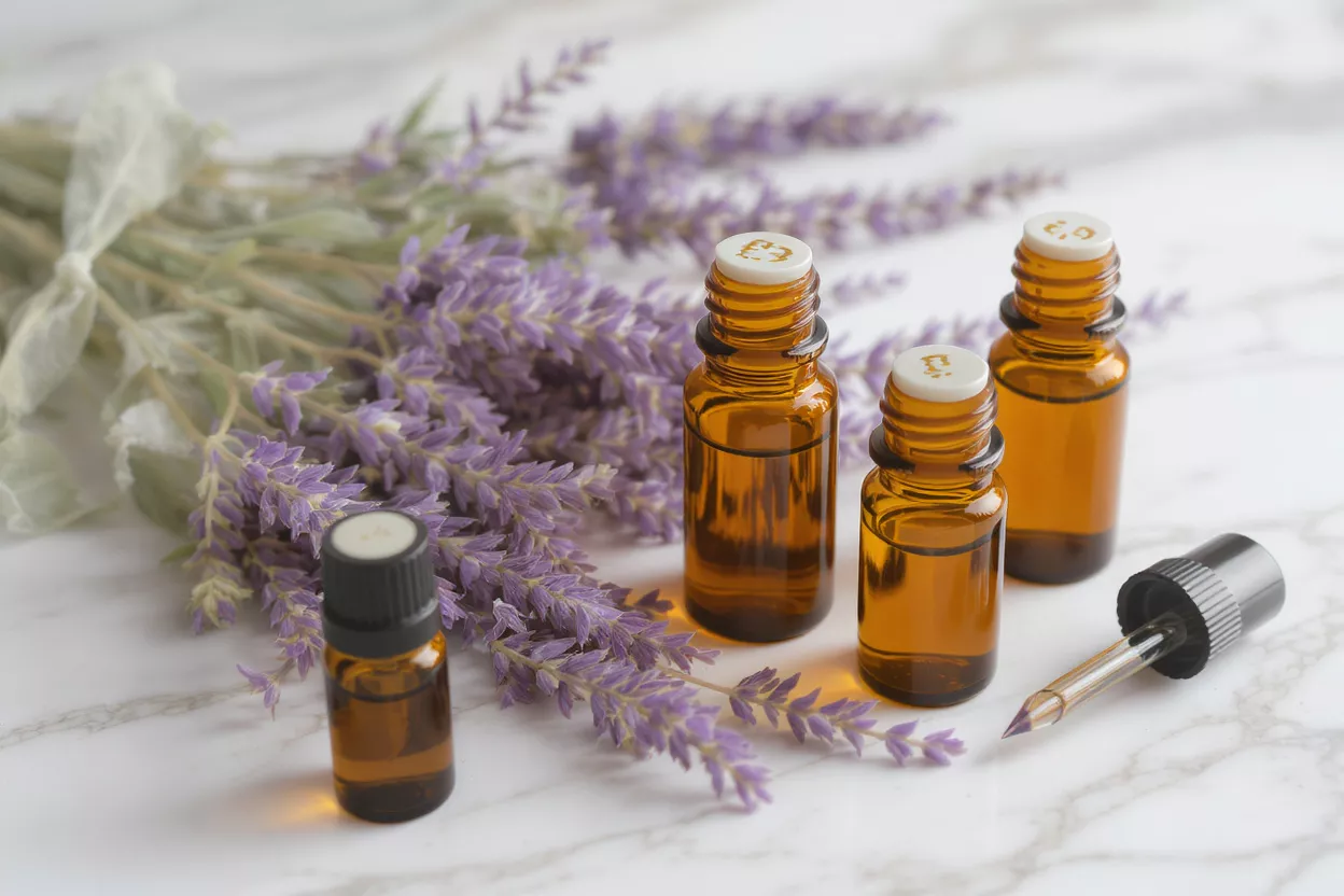 Amber essential oil bottles, one with a dropper, beside lavender on marble.