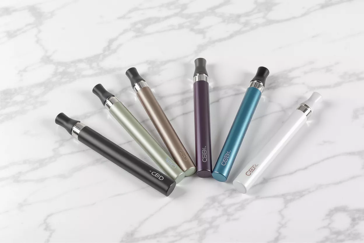 Six colorful CBD vape pens arranged on a white marble surface.