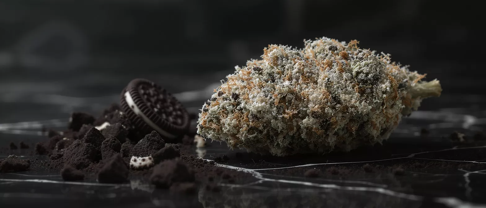 Close-up of a cannabis bud and Oreo cookie crumbs on a dark surface.