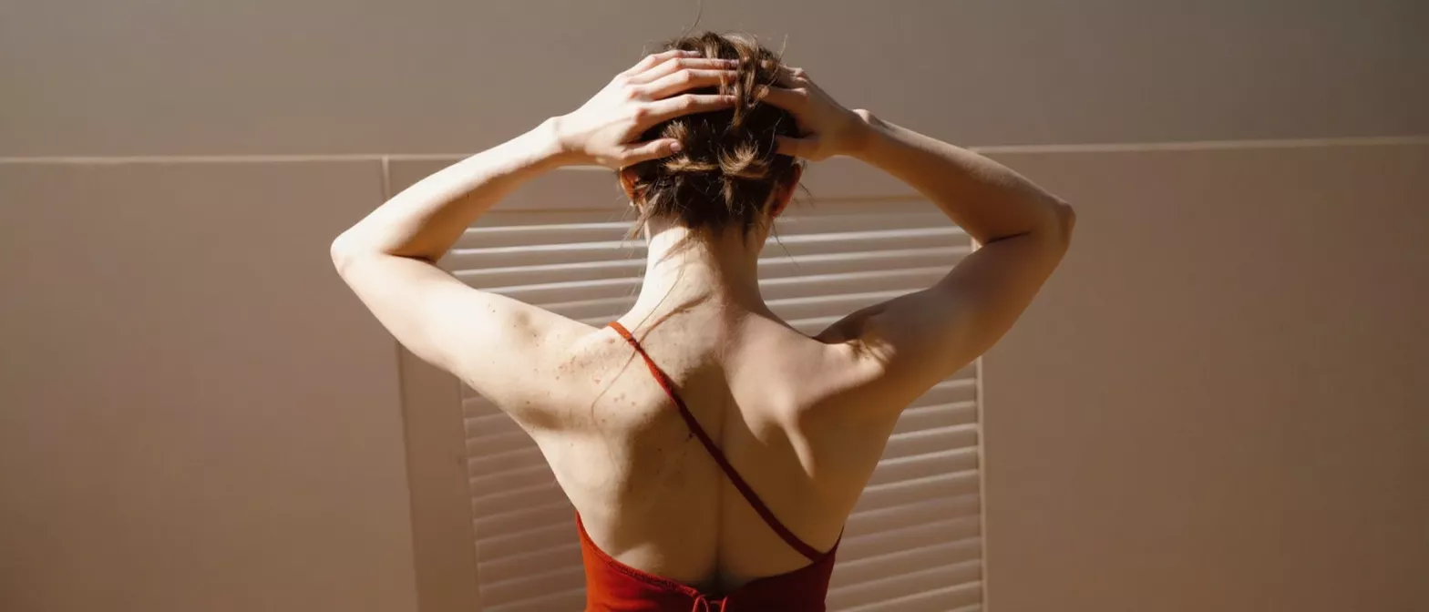 Back view of a woman in a red dress with hands in her hair.