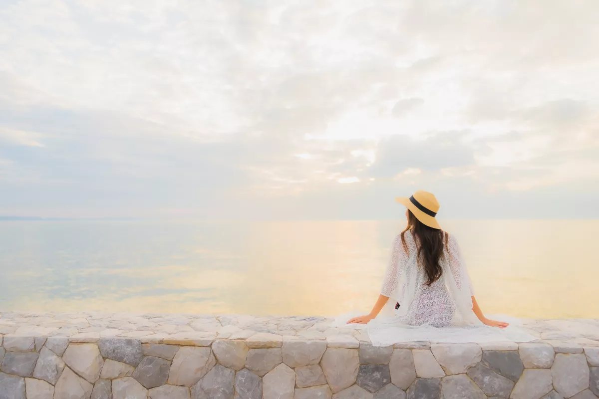 Person sitting on a wall, overlooking a serene lake during golden hour.