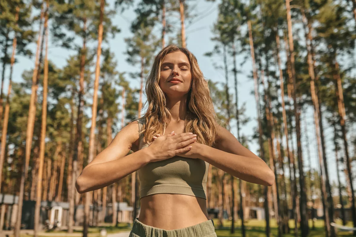 Woman in green meditating peacefully in serene pine forest setting.