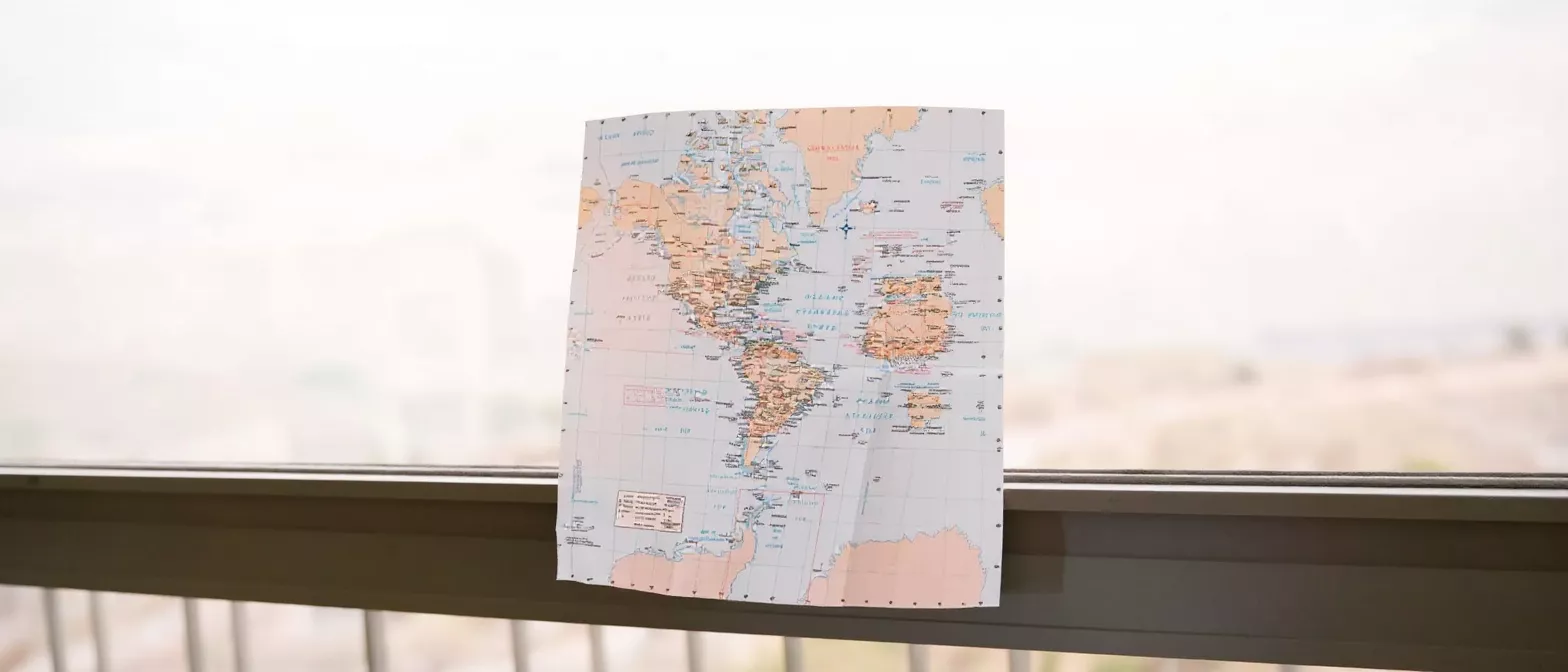 A folded world map hanging in a window, ready for travel planning.