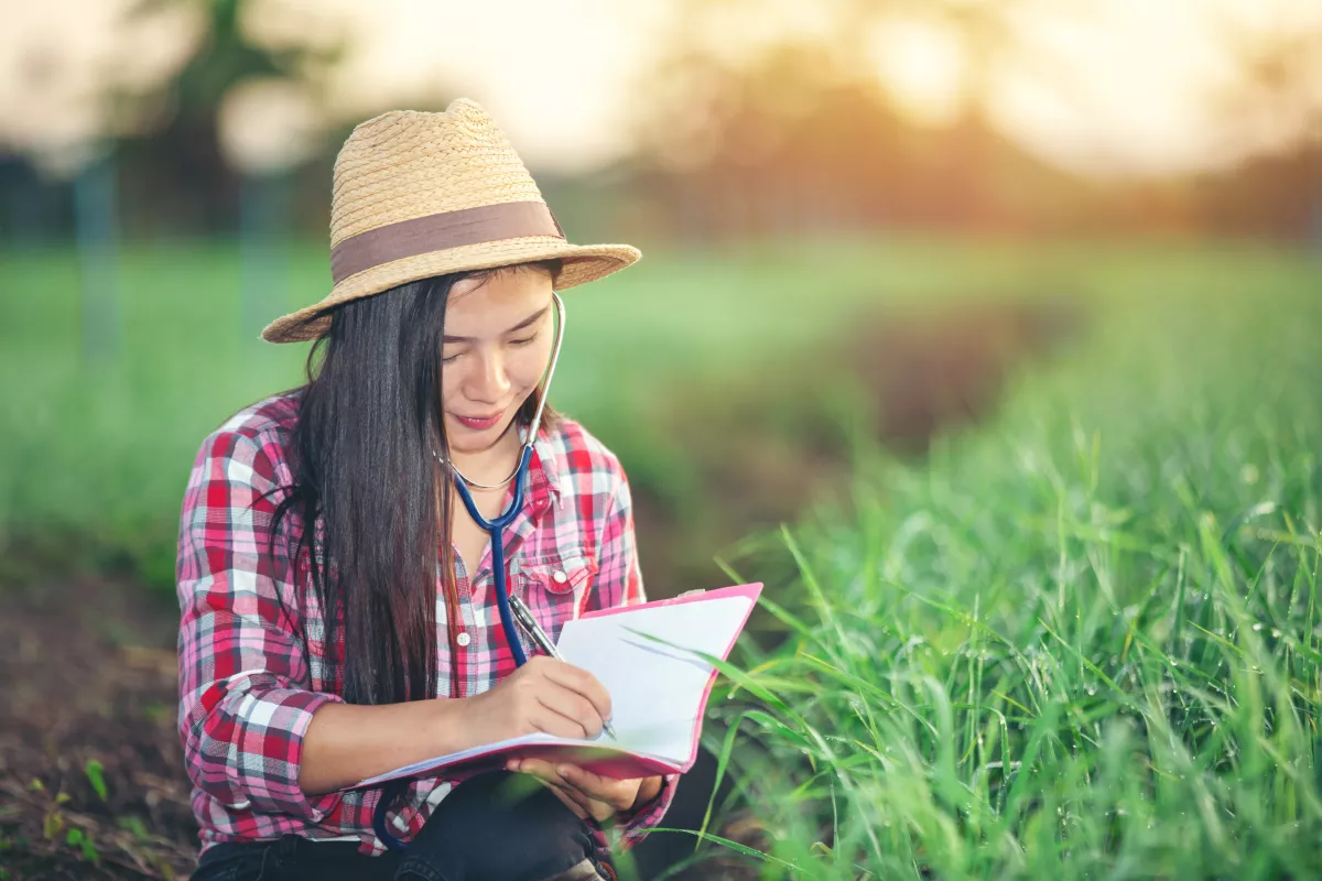 Medical student studying outdoors, wearing a hat, with stethoscope and pink notebook.
