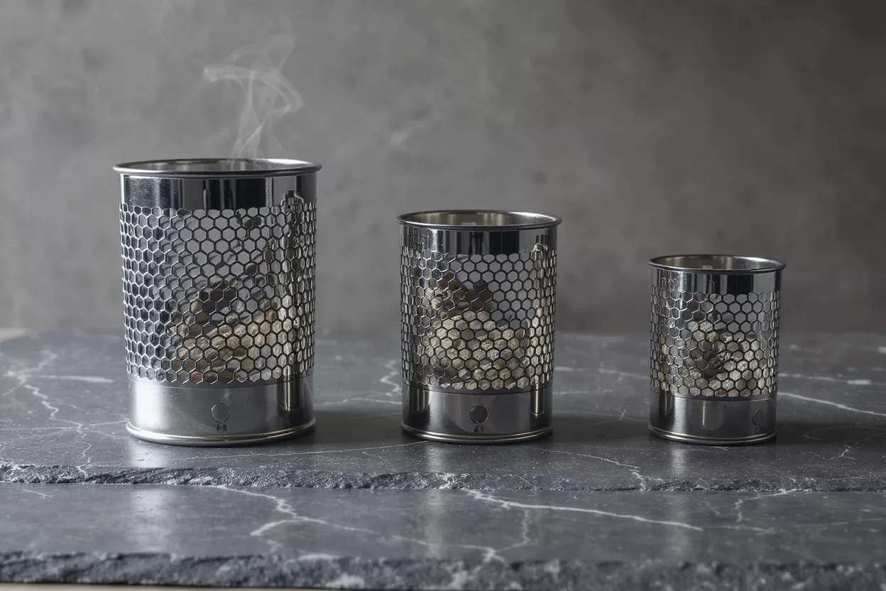 Three stainless steel tabletop smokers in different sizes on a dark slate surface.